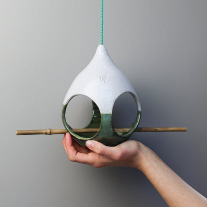 Hand holding ceramic green and white bird feeder with bamboo perch 